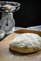 Fresh yeast dough on wooden board on dark background.