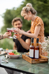 Young friends have a festive lunch outdoors, toasting and drinking wine, spending happy summer time together. Focus on a bottles with blank lables to copy paste on the table