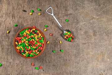 colored dragee with teaspoon in shape of shovel full of candies, on wooden background with copy...
