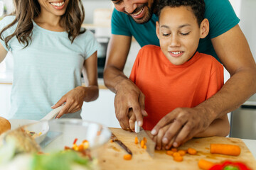Happy family cooking dinner together. Dad is showing his son how to chop a carrot while mom...