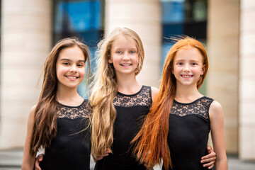 Portrait of three teenage girls with loose hair, blonde, redhead and brunette Summer on street. Vloses develop in wind.