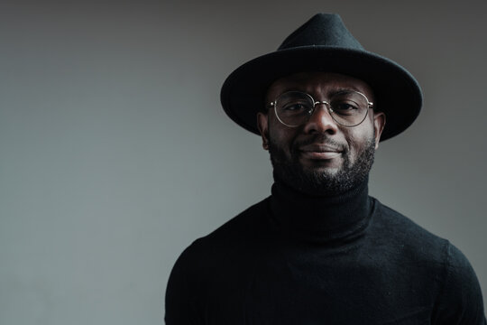 Handsome african american man in a hat wearing glasses and in a black turtleneck smiling looking at the camera