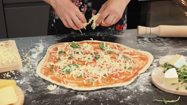 Female chef adding cheese on pizza base, preparing italian pizza margherita