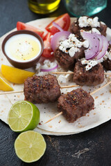 Close-up of bbq kofta kebabs with feta, white yogurt and tomatoes served on flatbread, vertical shot