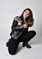 Fototapeta premium Full length portrait of young woman with natural brown hair, wearing black leather scifi outfit with jacket, standing pose on light studio background.