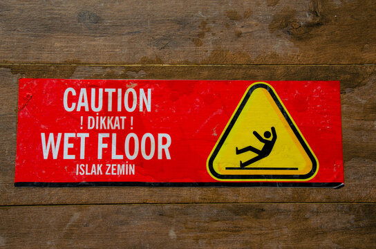 Red warning sticker for wet floor on brown tiled floor. The inscription on red information sticky label caution slippery floor in the hotel in Turkish "Dikkat! Islak zemin".