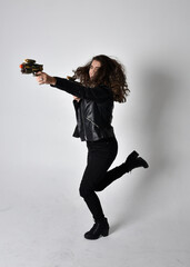 Full length portrait of young woman with natural brown hair,  wearing black leather scifi outfit with jacket, standing pose on light studio background.
