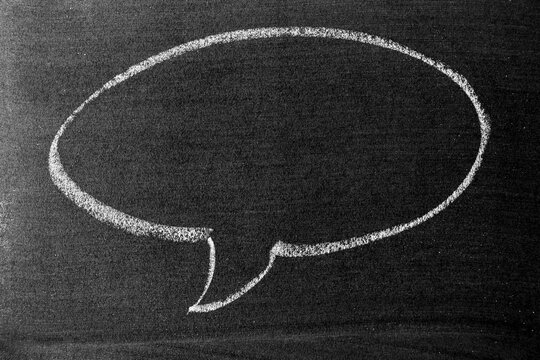 White color chalk hand drawing in round bubble speech shape with blank space on blackboard or chalkboard background
