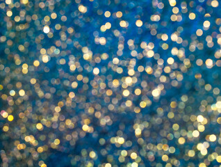 Abstract Christmas background of glittering round lights, real bokeh of lens blur. Soft sparkle pattern of gold and blue tints with defocused glow for holiday shiny wallpaper.
