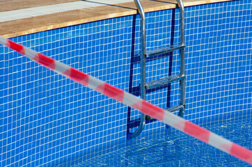 Selective focus on pool with no-entry tape. Red and white tape prohibits entry to swimming pool....