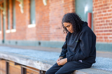 teenager dressed in black looking down sitting on platform