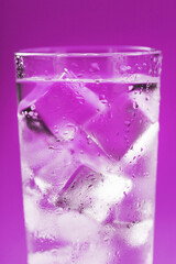 A glass with ice water and ice cubes on a blue background.