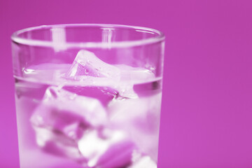 Glass with water and ice cubes on a pink background