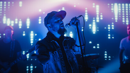 Fototapeta na wymiar Rock Band Performing at a Concert in a Night Club. Portrait of a Lead Singer Singing into Microphone. Live Music Party in Front of Bright Colorful Strobing Lights on Stage. 