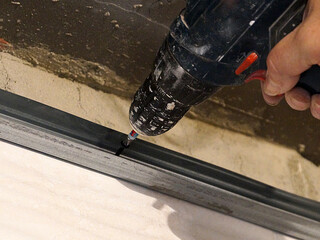 a man's hand fixes a drywall profile to the wall with a screwdriver