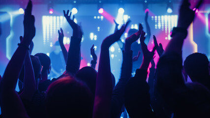Rock Band with Guitarists and Drummer Performing at a Concert in a Night Club. Front Row Crowd is...
