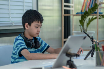Child boy is using communicates on the Internet at home. homeschooling, distant learning, Asian little boy taking a class online and happy for Homeschool Quarantine
