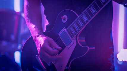 Fototapeta na wymiar Rock Band Performing at a Concert in a Night Club. Close Up Shot of a Five String Bass Guitar Played by a Musician. Live Music Party in Front of Bright Colorful Strobing Lights on Stage. 