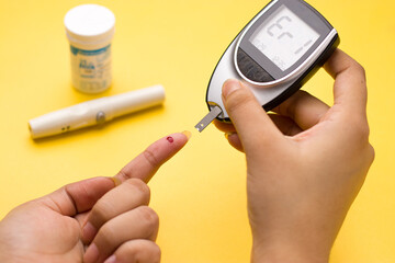 Blood glucose meter, the blood sugar value is measured on a finger on yellow background.