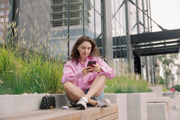 Portrait of young woman listening to music with mobile phone and relaxing while sitting on bus stop.