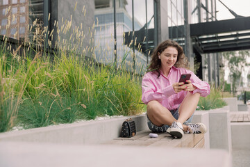 Portrait of young woman listening to music with mobile phone and relaxing while sitting on bus stop.