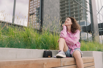 Portrait of young woman listening to music with mobile phone and relaxing while sitting on bus stop.