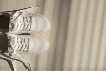 Close-up of women's white leather sneakers in the shade of the blinds.