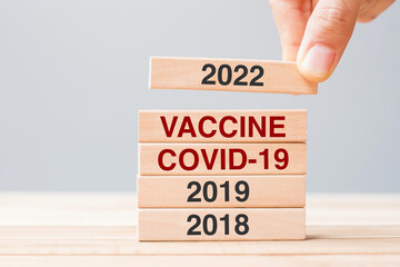 hand pulling 2022 block over Vaccine, COVID-19 and 2019 wooden building on table background. Crisis economy, Vaccination, immunization and Coronavirus ( Covid-19 ) pandemic