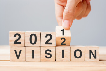 Businessman hand holding wooden cube and flip over block 2021 to 2022 VISION on table background. Resolution, plan, goal, mission, value and New Year holiday concepts