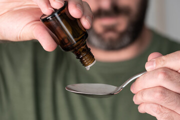 close-up of person dripping liquid medication drops onto spoon