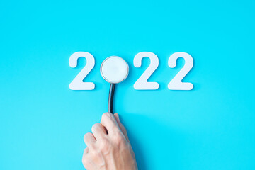 hand holding Stethoscope with 2022 number on blue background. Happy New Year for healthcare, Insurance, Wellness and medical concept
