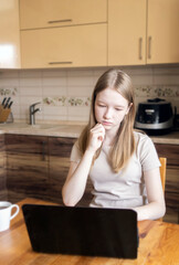 The girl looks at the laptop screen. Study at home, watch videos and online chat. A teenager in the kitchen.