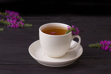 Cup of tea with willow-herb on wooden background.
