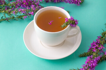 Cup of tea with willow-herb on mint background.