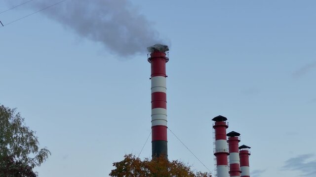 Chimney smoke / Smoke stack / Air pollution. Smoke comes from red-white chimneys on thermoelectric plant against sky...Unmodified camera color.