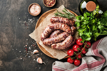 Raw sausages or bratwurst and ingredients for cooking on dark stone background. Top view with copy space.