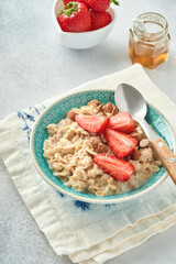 Oatmeal porridge with strawberry slices, nuts almonds and honey in blue bowl on grey table. Healthy eating, dieting, vegetarian food concept. Place for text