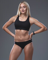 Fototapeta na wymiar Studio portrait of a young pretty girl with a sporty physique on a studio background. Beautiful blonde in a top and sports shorts. Sportswear for athletics.