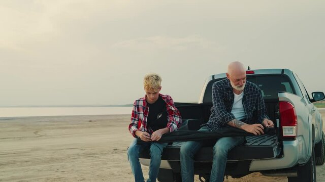 A handsome father with his son are unpacking a fishing rod sitting in a pickup truck while traveling on nature