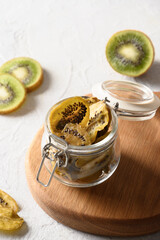 Fruits kiwi chips in glass jar on light background, home drying. Vegan free sugar food. Close up. Vertical format.