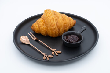 Croissant with mixed berry jam on black plate isolated on white background.