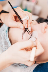 The master glues bunches of artificial eyelashes on the eyelids of a girl in a beauty salon