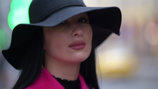 portrait of a brunette in a black hat and a pink coat against a background of blurred lights. close-up