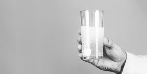 Glass of water tablet. Glass with efervescent tablet in water with bubbles. Close up of man holding a pill. Black and white