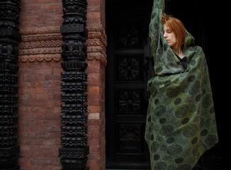 red hair woman in a cashmere scarf stands against the background of the door