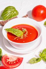 Bowls with homemade tomato soup. Ripe vegetables, fresh basil leaves, breadsticks, aromatic spices