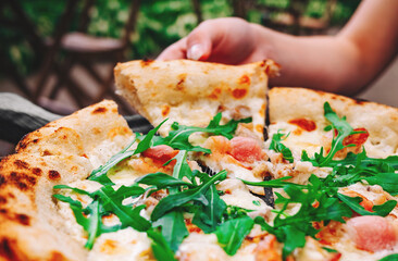 woman Hand takes a slice of meat neapolitan Pizza with Mozzarella cheese, ham, bacon, Spices and chicken in cafe outdoor