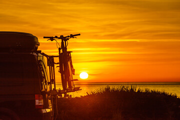 Camper with bicycles on rack camping on beach at sunrise
