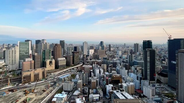 UMEDA, OSAKA, JAPAN : Aerial high angle sunset view of CITYSCAPE of OSAKA. View of buildings and street around Osaka and Umeda station. Wide view time lapse tracking shot, dusk to night.