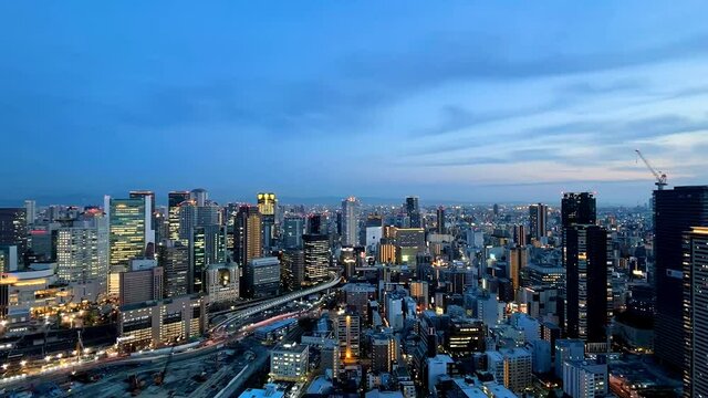 UMEDA, OSAKA, JAPAN : Aerial high angle sunset view of CITYSCAPE of OSAKA. View of buildings and street around Osaka and Umeda station. Wide view time lapse zoom in shot, dusk to night.